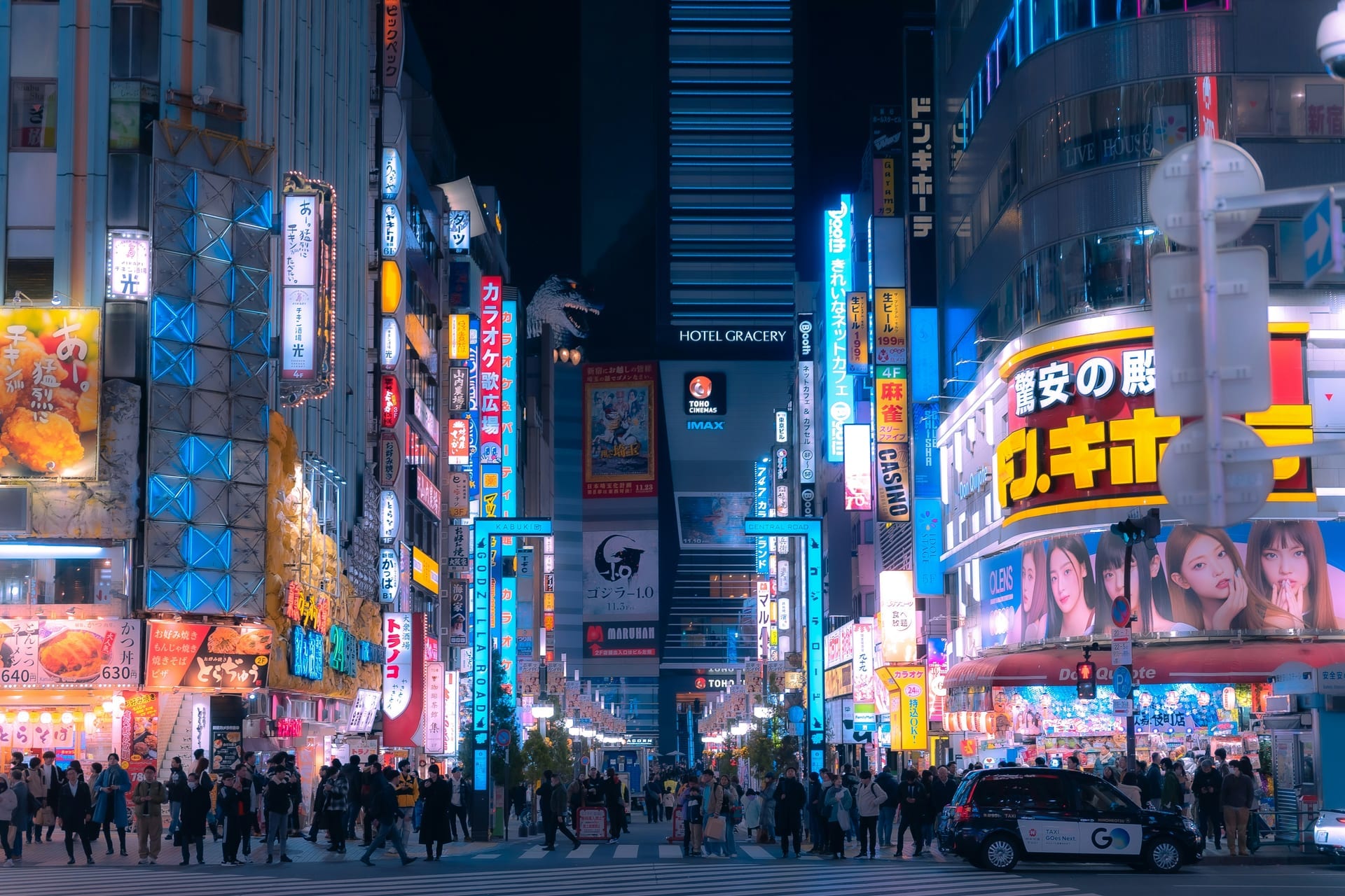 Wide view of Shinjuku's neon-lit entertainment streets at night with crowds and glowing billboards covering the buildings